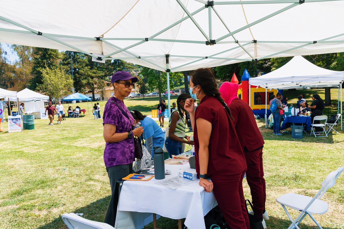 Wide view of the health fair with vendor tents, bounce house, and community members at Baldwin Village park